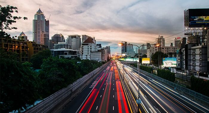 Photographie d’une voie rapide dans une ville, avec effets de lumières des phares des véhicules.